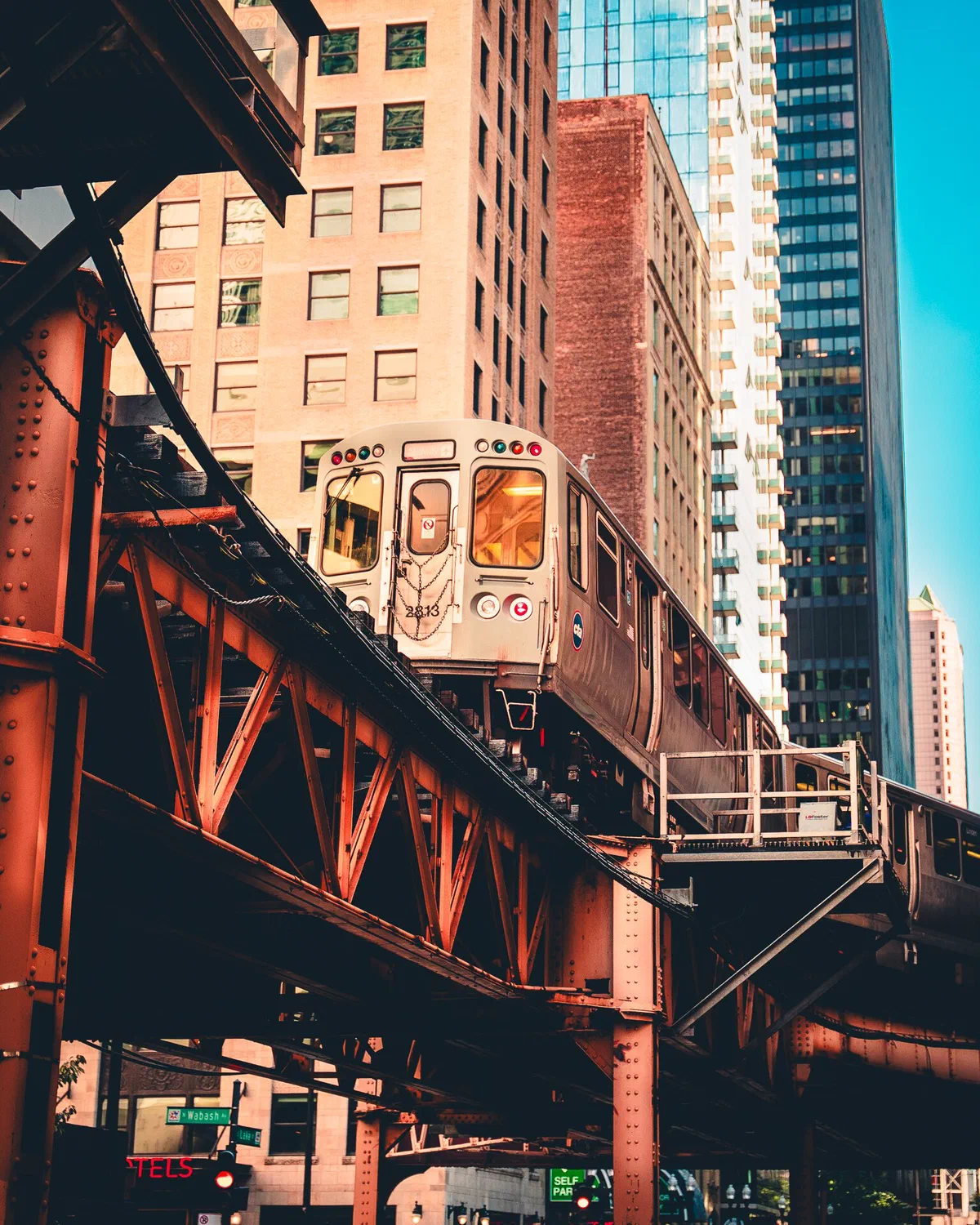 Un tren del L de Chicago avanza sobre la estructura de hierro elevada entre edificios altos, con el cielo azul a la derecha y un letrero de la calle Wabash abajo a la izquierda
