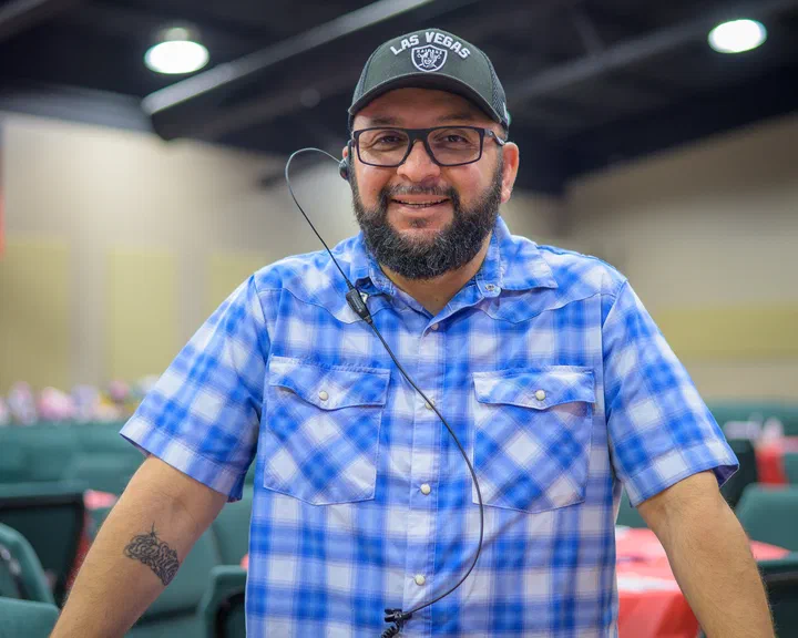 Eddie sonriente, con gorra, camisa a cuadros azul y micrófono de diadema