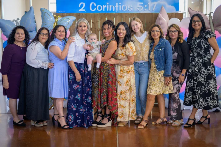 Un grupo de hermanas bajo el letrero “2 Corintios 5:17”; una con un bebé