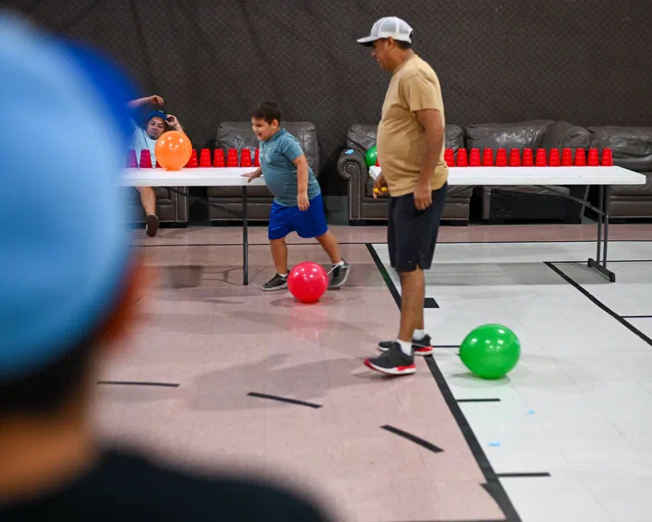 Un niño corriendo detrás de un globo rojo; al fondo, la mesa con vasos rojos