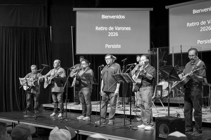 Músicos en la tarima; en las pantallas: “Bienvenidos, Retiro de Varones 2026, Persiste”