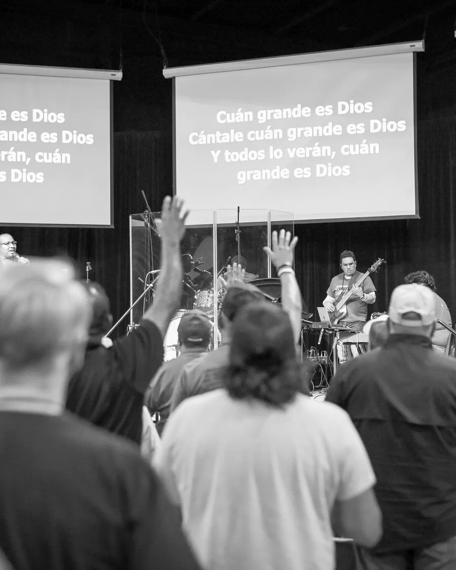 Hombres adorando con las manos en alto; en las pantallas se lee “Cuán grande es Dios”